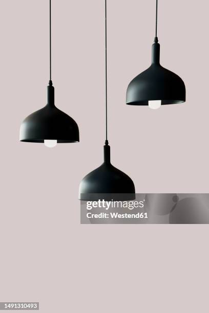 3d render of three black light fixtures hanging against pink background - pendant light stock illustrations