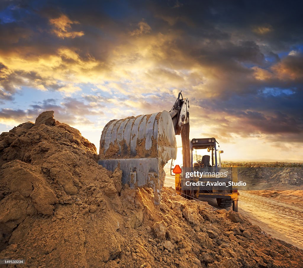 Excavator on the construction site of the road against the setting sun