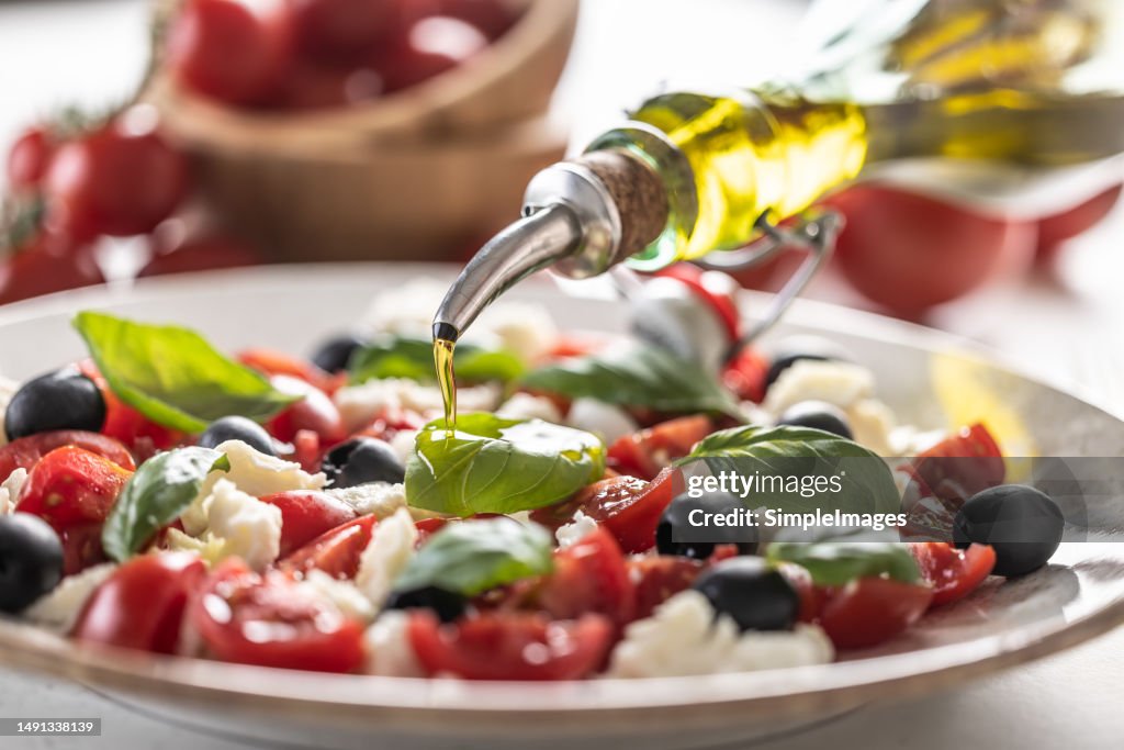 Close-up of pouring olive oil into an Italian Caprese salad. Mediterranean vegetarian appetizer with olive oil.