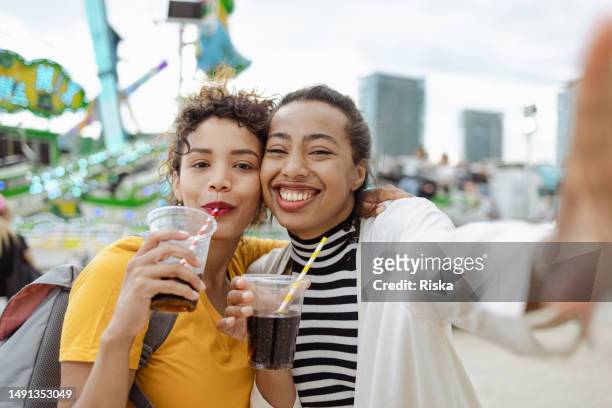 cheerful multiracial women are feeling happy while drinking at the amusement park. they are looking at the camera and smiling. - park festival bildbanksfoton och bilder