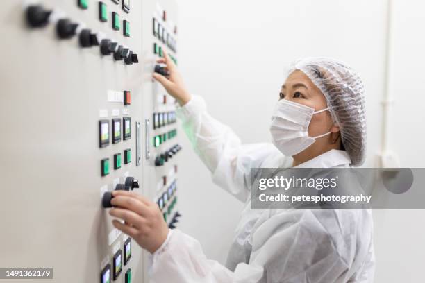 a female in full white clean suit operating a switch control panel - pharmaceutical factory stock pictures, royalty-free photos & images
