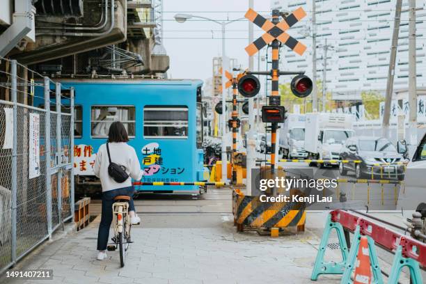 rear view of an asian woman riding a bike commuting in the city, waiting for crossing railway track before a train passing through. - cross railway station stock pictures, royalty-free photos & images