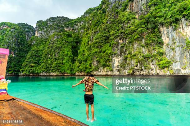 a man jumps into the sea from a longtail boat at pileh lagoon. a bay surrounded by mountains and emerald green sea at koh phi phi. krabi province, thailand - phuket province stockfoto's en -beelden