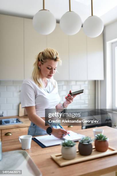 beautiful blond female writing down recipe while getting it over the phone - lady cooking confused imagens e fotografias de stock