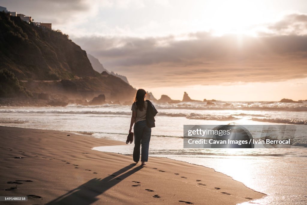 Young woman walking at a black sand beach at sunset