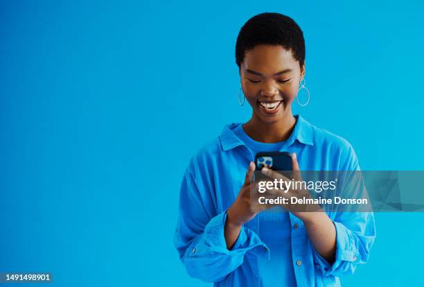 young black woman standing and looking at her mobile phone, whilst smiling as she responds back to a text message wearing casual clothing with copy space, stock photo - woman looking down smiling stock pictures, royalty-free photos & images