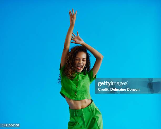 young multiracial woman dancing moving side to side wearing a green shirt and green pants with her eyes closed and  arms raised, shot against a blue background with copy space, stock photo - swaying stock pictures, royalty-free photos & images