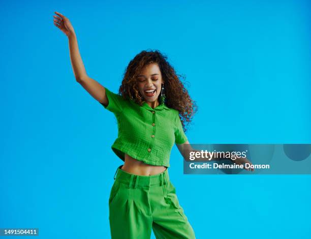 beautiful young dancing multiracial woman swaying side to side wearing a green shirt and green pants with her eyes closed and arms raised, shot against a blue background with copy space, stock photo - dancing funny carefree woman stock pictures, royalty-free photos & images