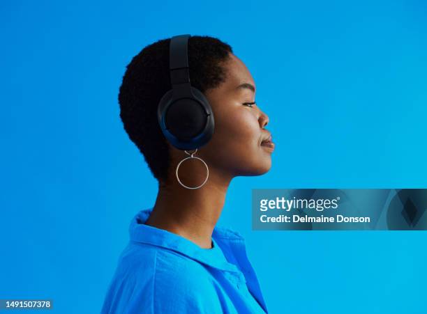 side view of a young black woman standing whilst listening to music on her headphones with copy space, stock photo - blue backgrounds stock pictures, royalty-free photos & images