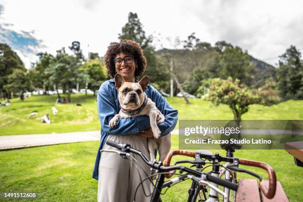 mujer joven sosteniendo un bulldog francés en brazos en un parque público - perro faldero fotografías e imágenes de stock