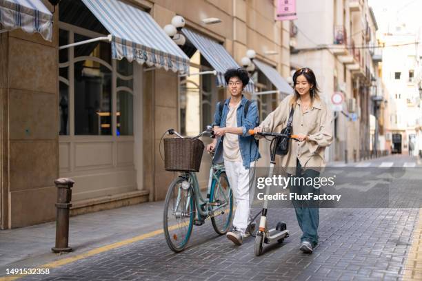 asian female and male students, commuting together with bicycle and electric push scooter - sustainable transportation stock pictures, royalty-free photos & images