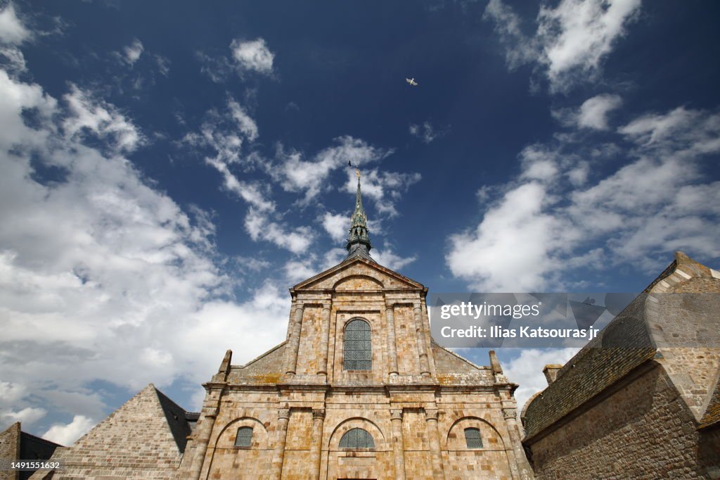 Sunlit façade of the church-abbey Saint-Michel against a cloudy blue sky