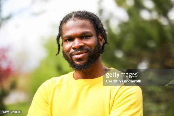portrait of young black man in yellow shirt with african braided hair in front of green background - rastafarian stock pictures, royalty-free photos & images