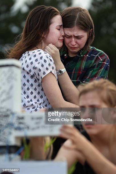 Two daughters of movie-theater-shooting-victim Gordon Cowden's embrace one another as another daughter leave messages on a cross at the makeshift...