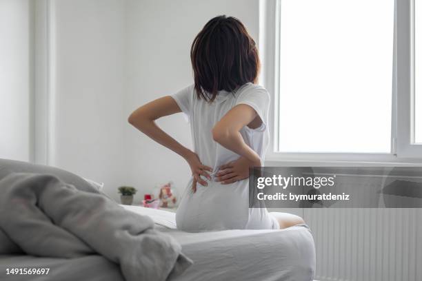 woman feels back pain massaging aching muscles - back pain bed stock pictures, royalty-free photos & images