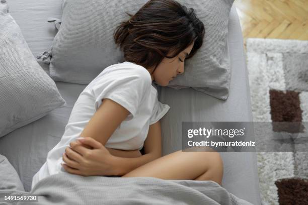 woman suffering abdominal pain touching aching stomach while lying in bed - urinewegstelsel stockfoto's en -beelden