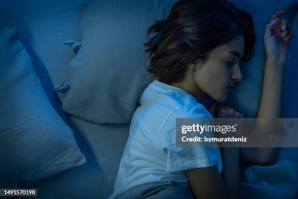 woman sleeping cozily on a bed in her bedroom at night - woman sleeping on mattress stock pictures, royalty-free photos & images