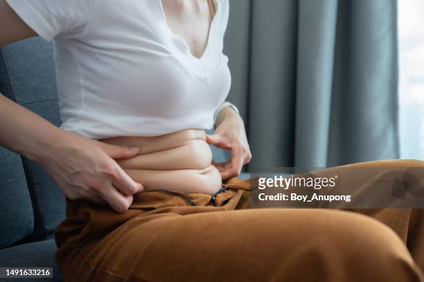 cropped shot of woman touching and squeezing her fat belly. - mala postura fotografías e imágenes de stock