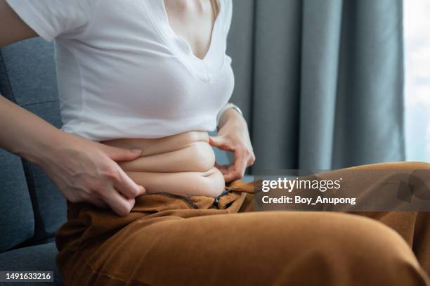 cropped shot of woman touching and squeezing her fat belly. - fat foto e immagini stock