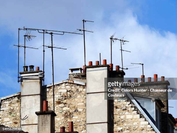 old rake antennas and chimneys on the roof of a residential building and cloudy sky in paris, france - technofobie stockfoto's en -beelden