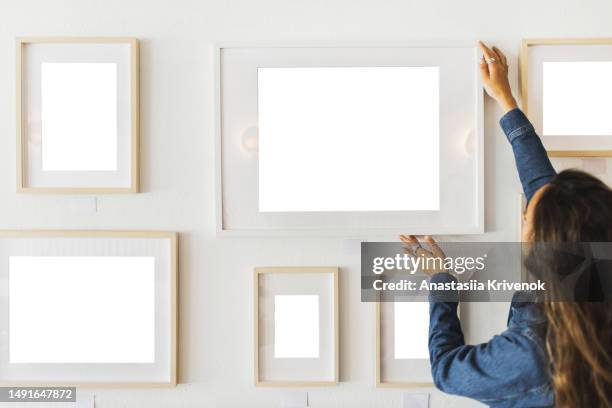 woman hanging picture frame on wall. - hanging picture frame stock pictures, royalty-free photos & images