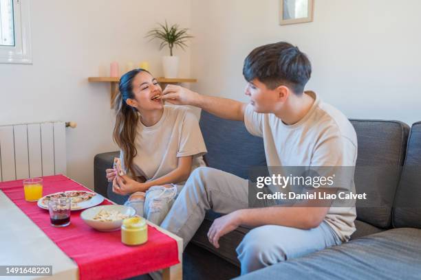 happy young couple having fun while eating pizza and nachos chips at home. - casa calvet stock pictures, royalty-free photos & images