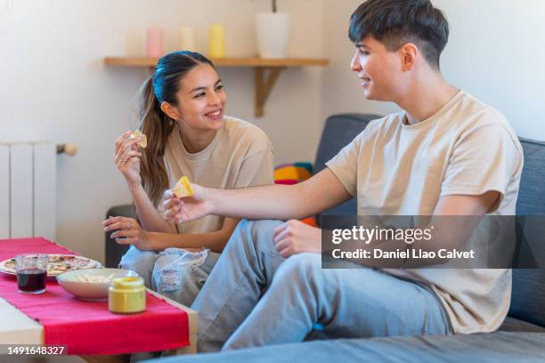 young couple enjoying eating together on the sofa at home. - casa calvet stock pictures, royalty-free photos & images