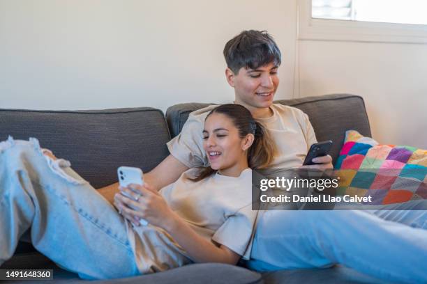 young couple using their mobile phones while relaxing on the sofa at home. - casa calvet stock pictures, royalty-free photos & images