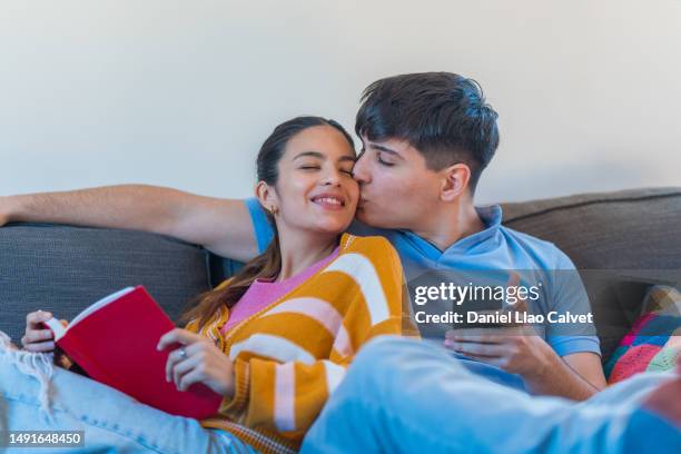 man kissing his girlfriend while relaxing on the sofa together. - casa calvet stock pictures, royalty-free photos & images