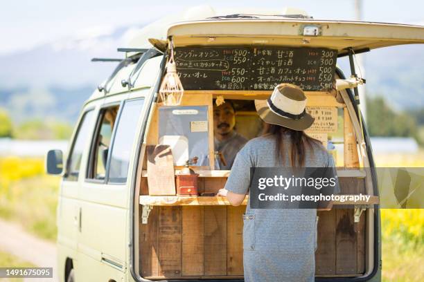 a woman buys coffee from a mobile coffee van in the countryside amongst a sea of yellow flowers - iwate prefecture stock pictures, royalty-free photos & images