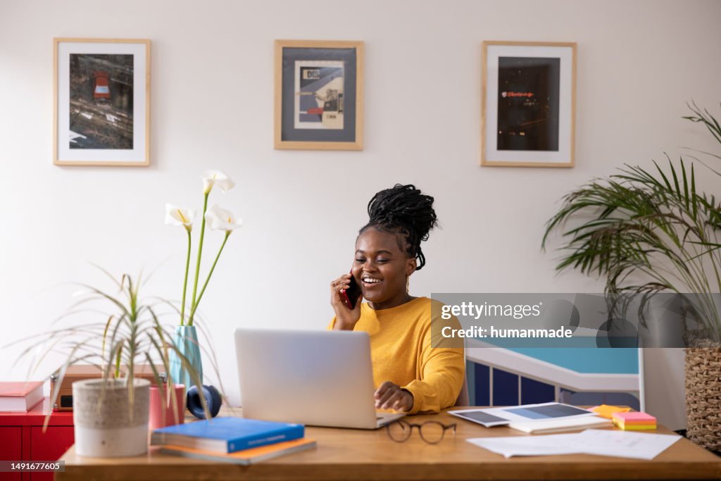 Young African American woman talking on her smart phone and working at home