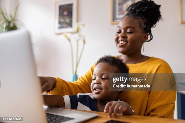 black mother working from her home office with her toddler son in her lap - freelance child stock pictures, royalty-free photos & images