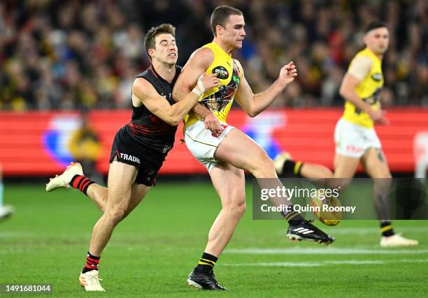 Jack Ross of the Tigers kicks whilst being tackled by Zach Merrett of the Bombers during the round 10 AFL match between Essendon Bombers and Richmond...