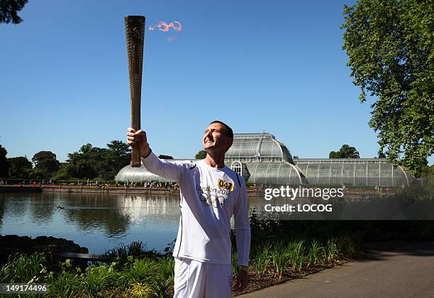 In this handout image provided by LOCOG, Torchbearer 047 John Harding holds the Olympic Flame on the Torch Relay leg through Kew Gardens on July 24,...