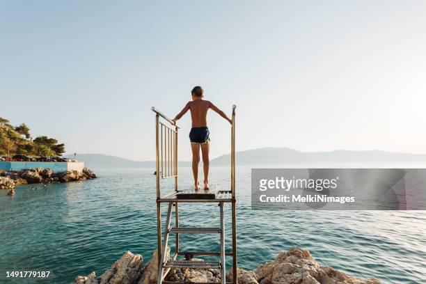 young boy climbing on a diving platform and prepare to jump in to the sea - albania stock pictures, royalty-free photos & images