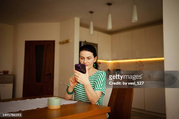 a woman, 40-45 years, sitting at dining table having coffee and looking at mobile phone - 40 44 years woman stock-fotos und bilder