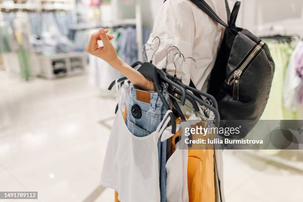 unrecognizable lady in white blouse with black backpack carrying selected clothes to try on - shopping bag in hand stockfoto's en -beelden
