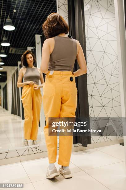 slim mature lady standing in front of mirror trying on orange pants and brown top - full length mirror fotografías e imágenes de stock