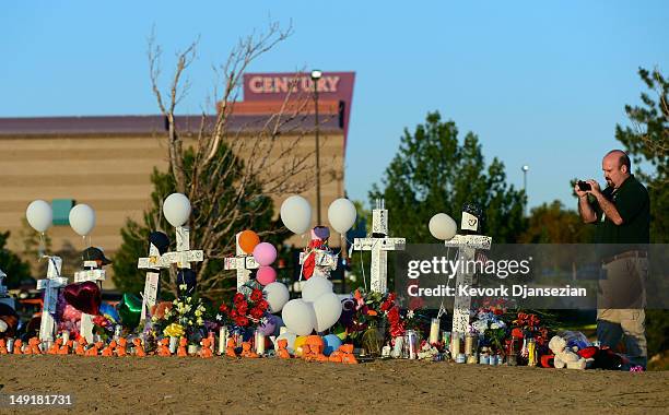 Aurora city employee Demetrius Romo-Gilmore takes a photograh of a makeshift memorial to the 12 movie theater shooting victims built across the...