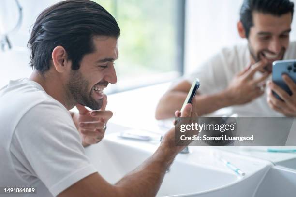 man looking in smartphone in front of sink in bathroom. - brush teeth phone stock pictures, royalty-free photos & images