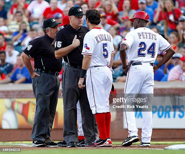 Gary Pettis of the Texas Rangers looks on as Ian Kinsler disputes a call by umpire Tim Tschida to umpire Jeff Nelson on first base which resulted in...