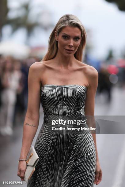 Annika Gassner seen a silver long shimmery black and white long dress, YSL Logo beige clutch and heels during the 76th Cannes film festival on May...