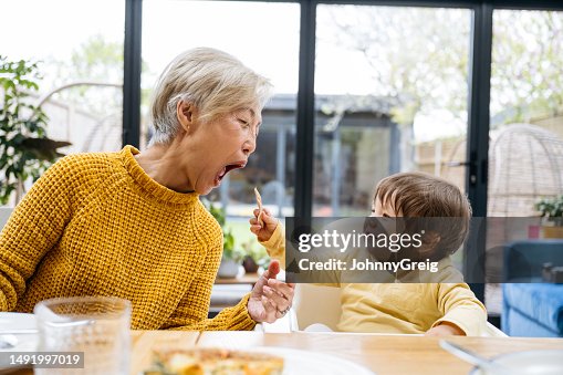 Baby grandson feeding his grandmother at dining table Baby grandson feeding his grandmother at dining table