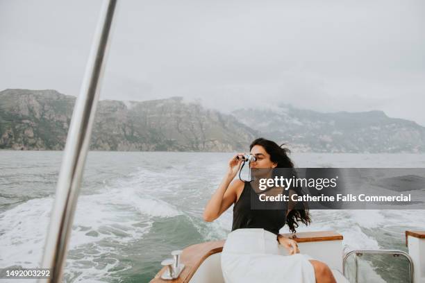 a beautiful indian woman reclines on the stern of a small luxury yacht, and looks through a pair of small binoculars, and gazes out to sea. - passagier wasserfahrzeug stock-fotos und bilder