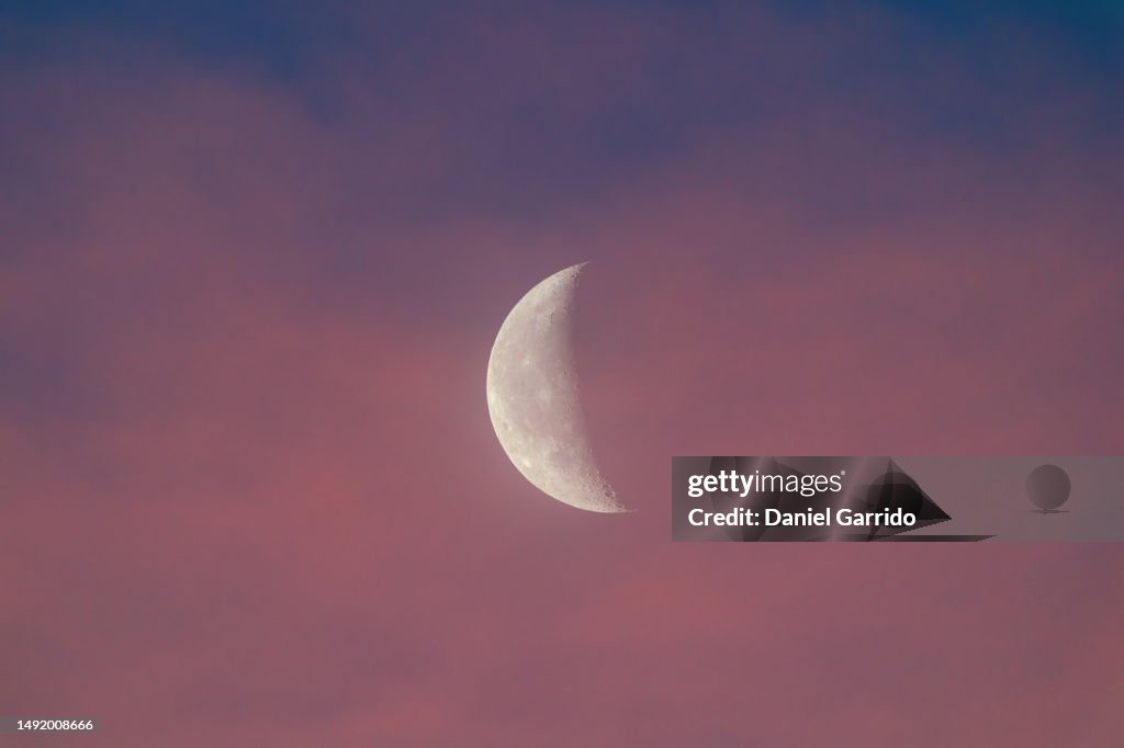 Nighttime beauty, the half moon reveals its craters amidst orange clouds at dusk