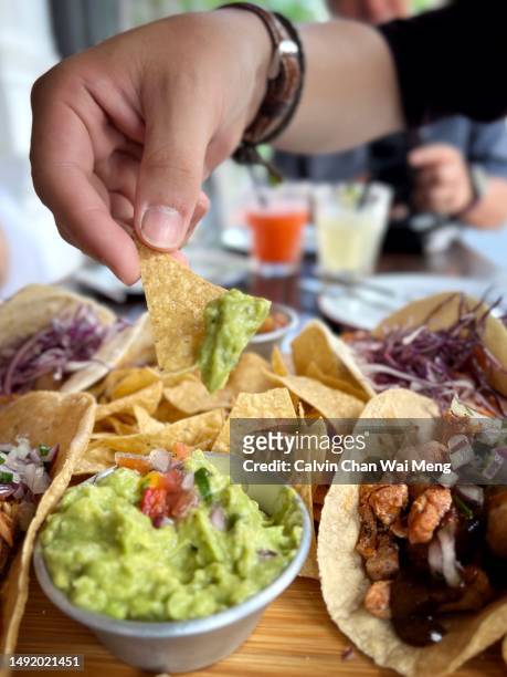 adult hand dipping nacho corn chips with guacamole sauce - saturated fat stock pictures, royalty-free photos & images