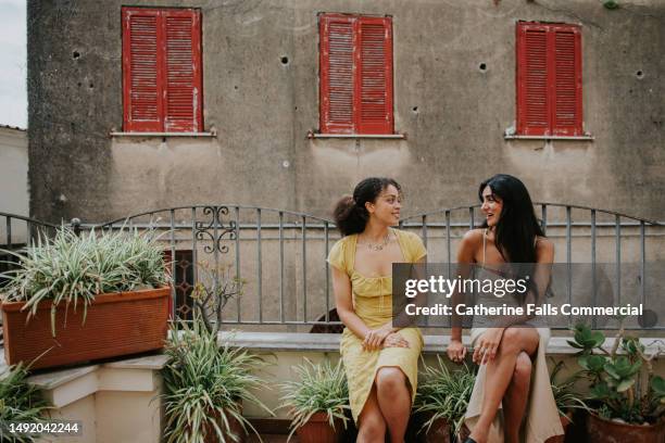 two beautiful woman have a casual conversation on a balcony - zuid europa stockfoto's en -beelden