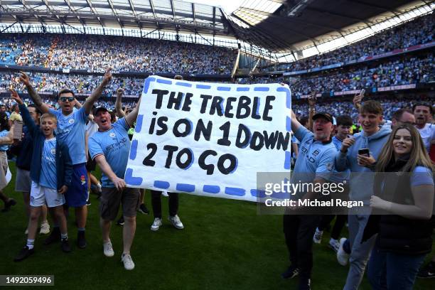 Fans of Manchester City hold a sign which reads "The Treble Is On, 1 Down, 2 To Go" as they invade the pitch after the final whistle of the Premier...