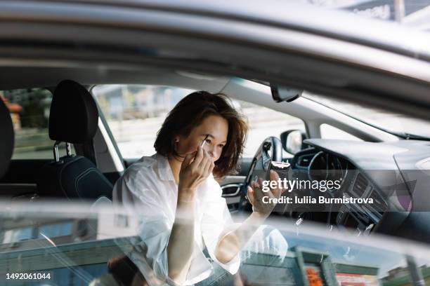 beautiful asian woman with brown hair applying makeup sitting in car - eyebrow pencil fotografías e imágenes de stock
