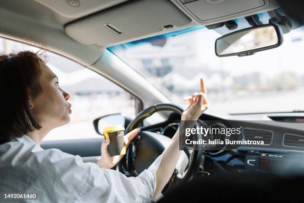 mature business woman of mongolian ethnicity in white shirt making obscene gesture while driving car - road rage stock pictures, royalty-free photos & images